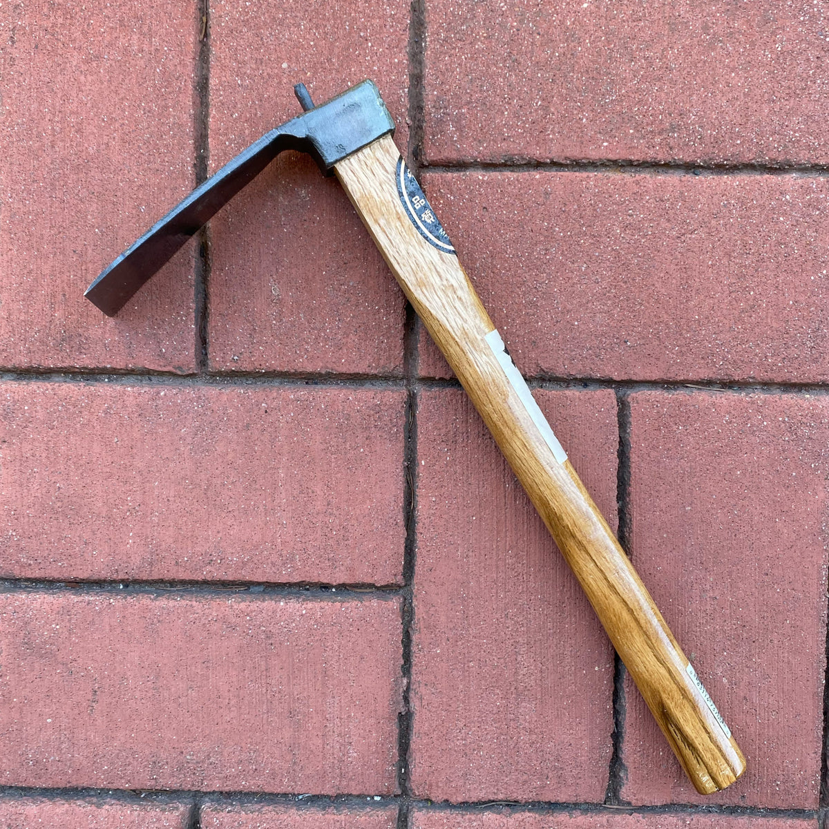 A black metal hoe with a wooden handle. It is sitting on red bricks.