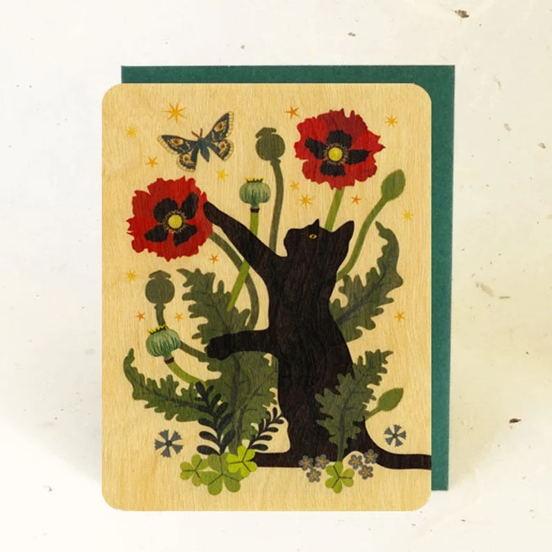A wooden card with a black cat and colorful red poppy flowers.