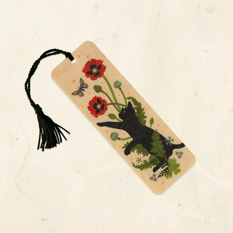 A wooden bookmark with a black cat and colorful red poppy flowers. It has a black tassel. 