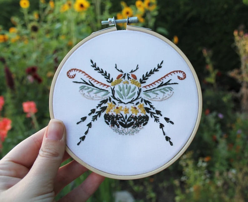 A hand holding up a completed version of this design. It has a bee whose body is made up of different flowers and plant parts.