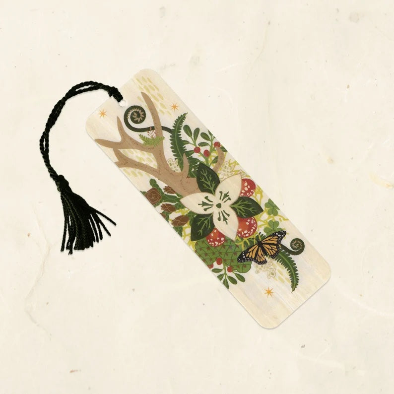 A wooden bookmark with a forest garden and a monarch butterfly. It has a black tassel. 