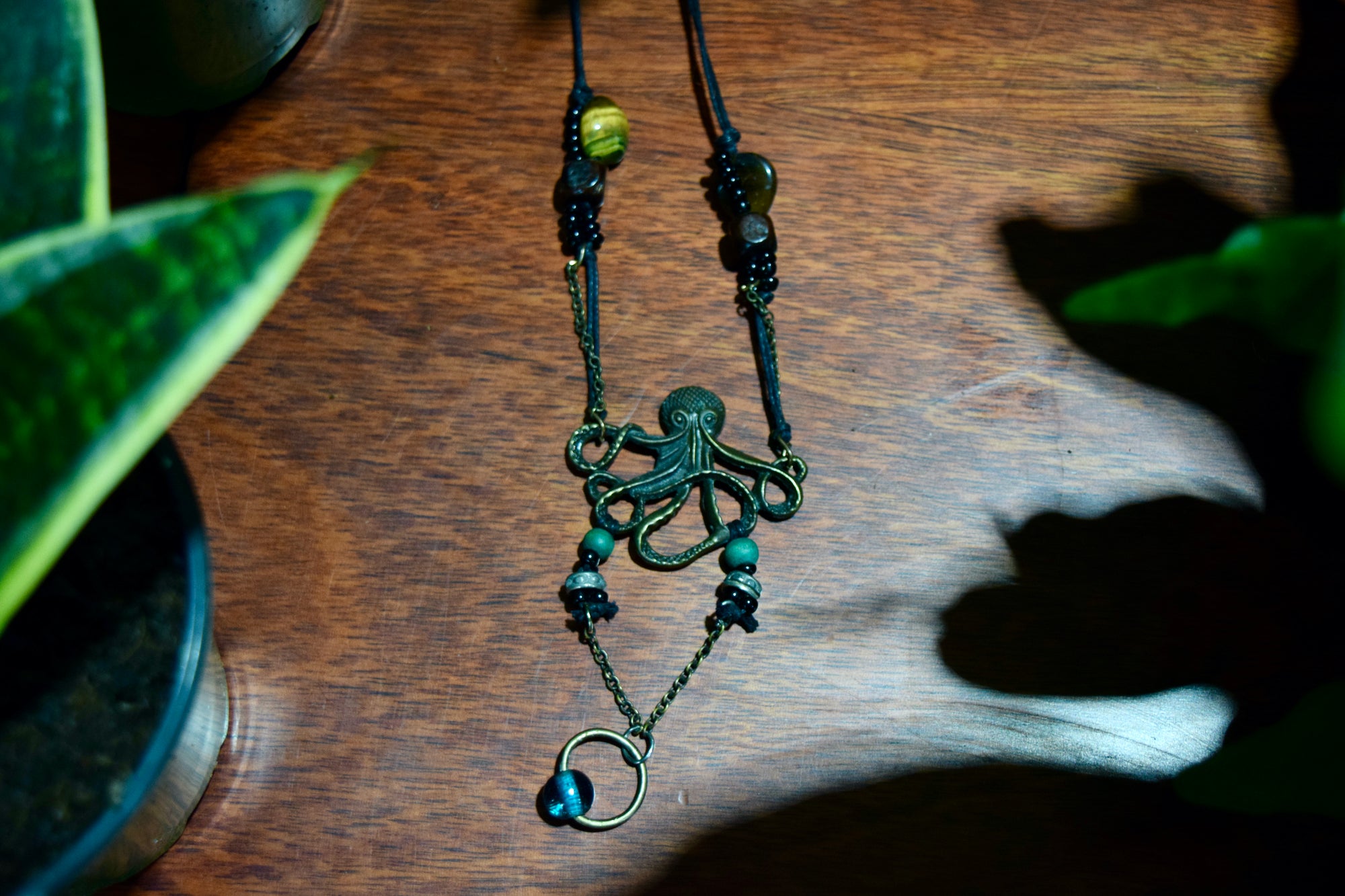 The octopus neckless on a dark wooden surface, surrounded by plants.