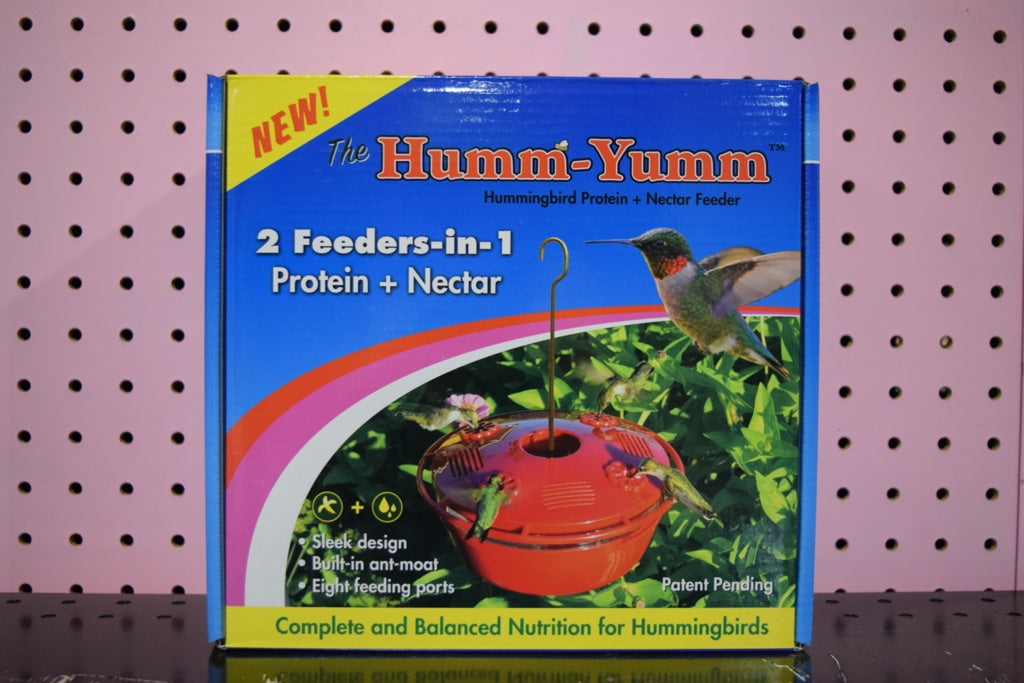 A Humm Yumm feeder in a blue box. The box shows a red circular feeder with 4 hummingbirds, one on each side.