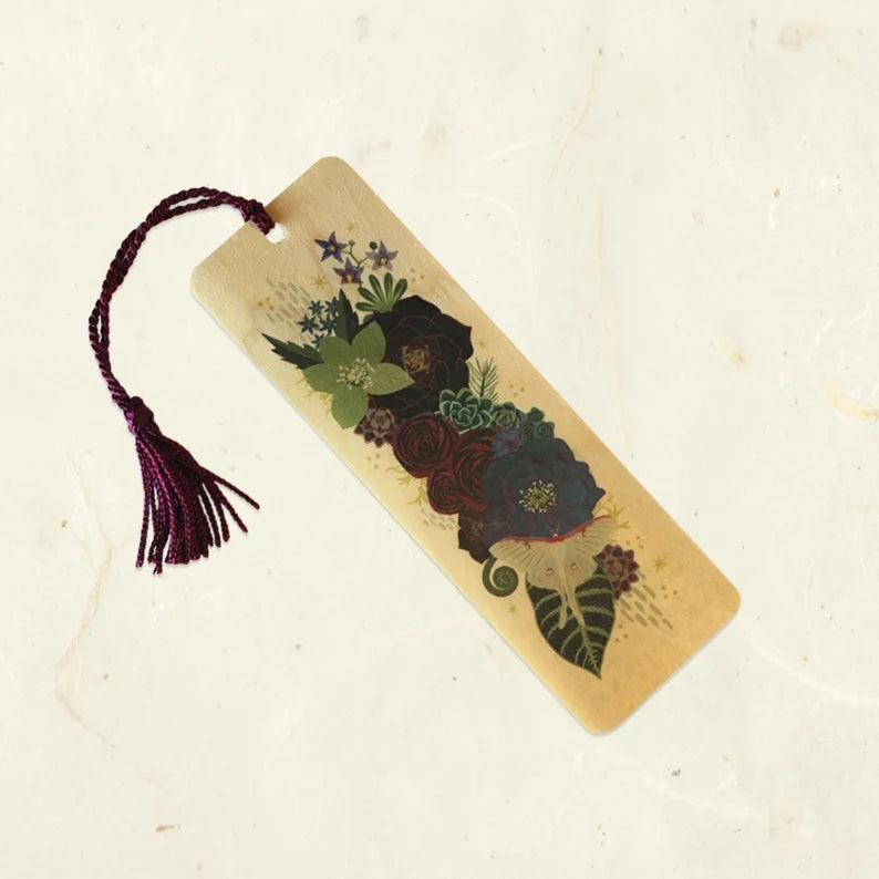 A wooden bookmark with various dark-colored flowers and a white luna month. The tassel is burgundy. 
