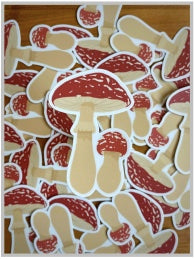 Multiple Amanita muscaria mushroom stickers are visible. One in the center shows that each sticker has a large and small mushroom. They are cream colored with red and white caps.