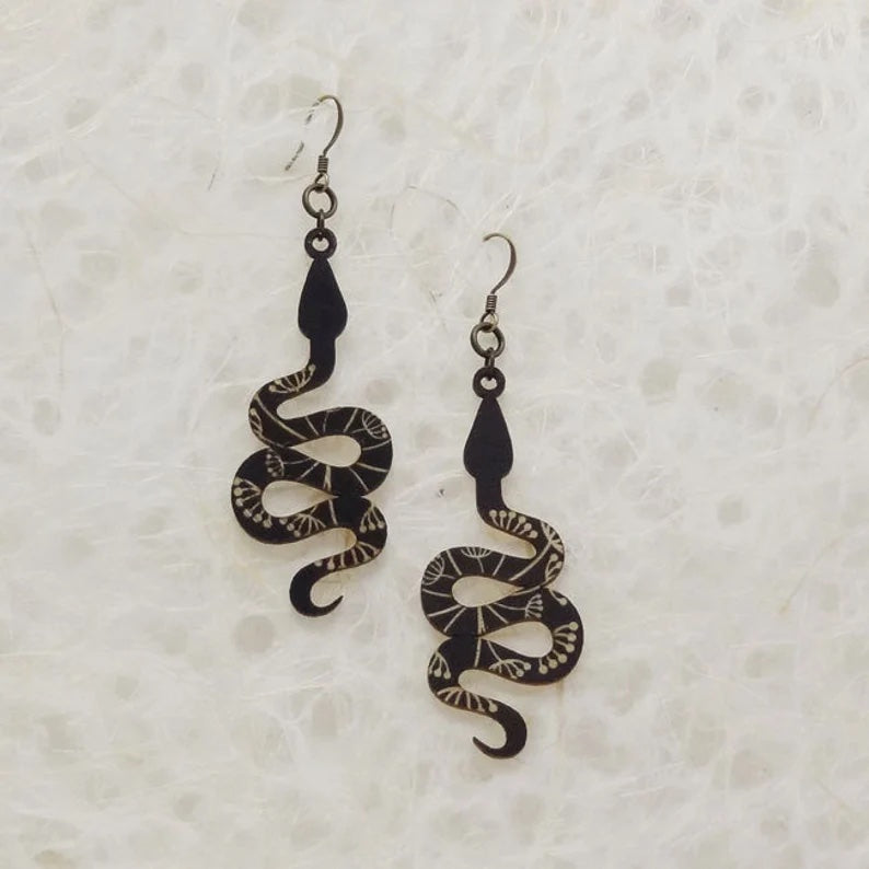 Black dangling snake earrings. A white floral pattern is etched into the black wood.
