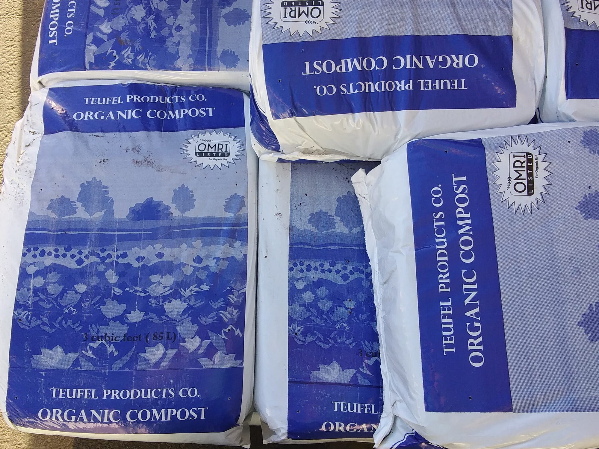 Large blue and white bags of compost stacked on each other.